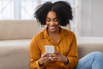Smiling millennial curly african american woman typing on phone, watch video