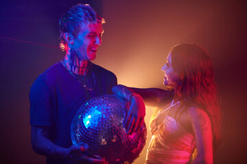 Happy young couple with disco ball standing on dance floor in night club and looking at each other
