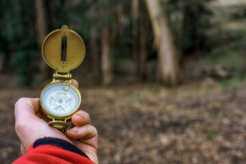 a man's hand holds a compass to orient himself in a forest