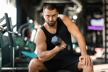 Fototapeta na wymiar Young Muscular Man Doing Exercises With Dumbbell In Modern Gym