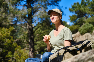 Young woman with backpack sitting in park while eating sandwich
