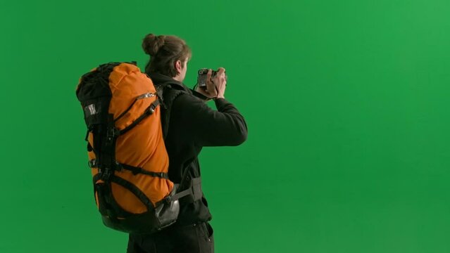 Back view of a male traveler taking photos on a camera during a hike. A male traveler stands in a studio on a green screen close up. Concept of travel, active rest, hiking.