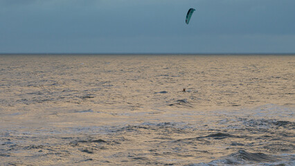 Kitesurfing. Kiteserferzy o zachodzie słońca na tle złocistego morza. Silny wiatr tworzy...