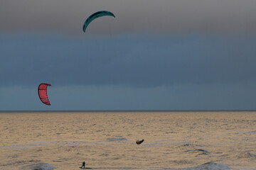 Kitesurfing. Kiteserferzy o zachodzie słońca na tle złocistego morza. Silny wiatr tworzy doskonałe warunki do powietrznych ewolucji. Pastelowe kolory, low key.