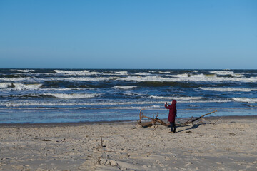 Spacer w sztormową, słoneczną pogodę. Brzeg morza przesunął się. Morze zabrało dużą część plaży. Kobieta spaceruje i robi zdjęcia.