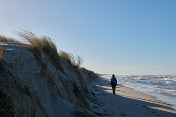 Spacer w sztormową, słoneczną pogodę. Brzeg morza przesunął się. Morze zabrało dużą część plaży. Kobieta spaceruje i robi zdjęcia.