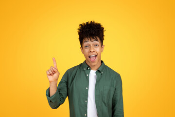 Excited african american guy raising finger up, yellow background
