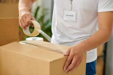 Cropped image of volunteer taping boxes in office of charity organization