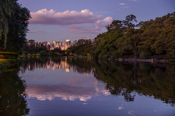 Ibirapuera, zona sul da cidade de São Paulo, ao anoitecer, com reflexo da cidade em lago.