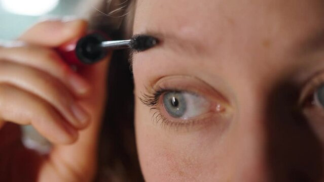 Detailed image of a woman carefully applying mascara to her eyelashes, enhancing her natural beauty. A woman paints her eyebrows, prepares for a date or a business meeting, body care, cosmetology