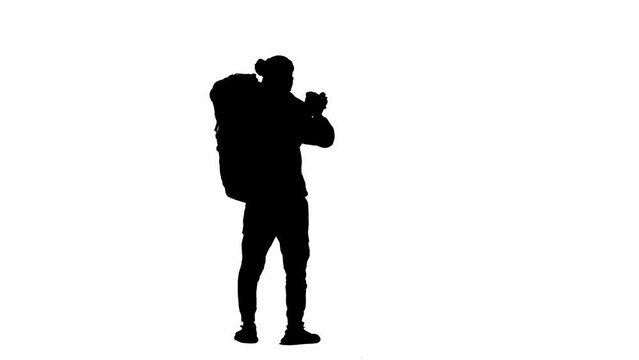 Black silhouette of a male traveler taking photos on a camera during a hike. A male traveler stands on white isolated background. Concept of travel, active rest, hiking. Rear view.