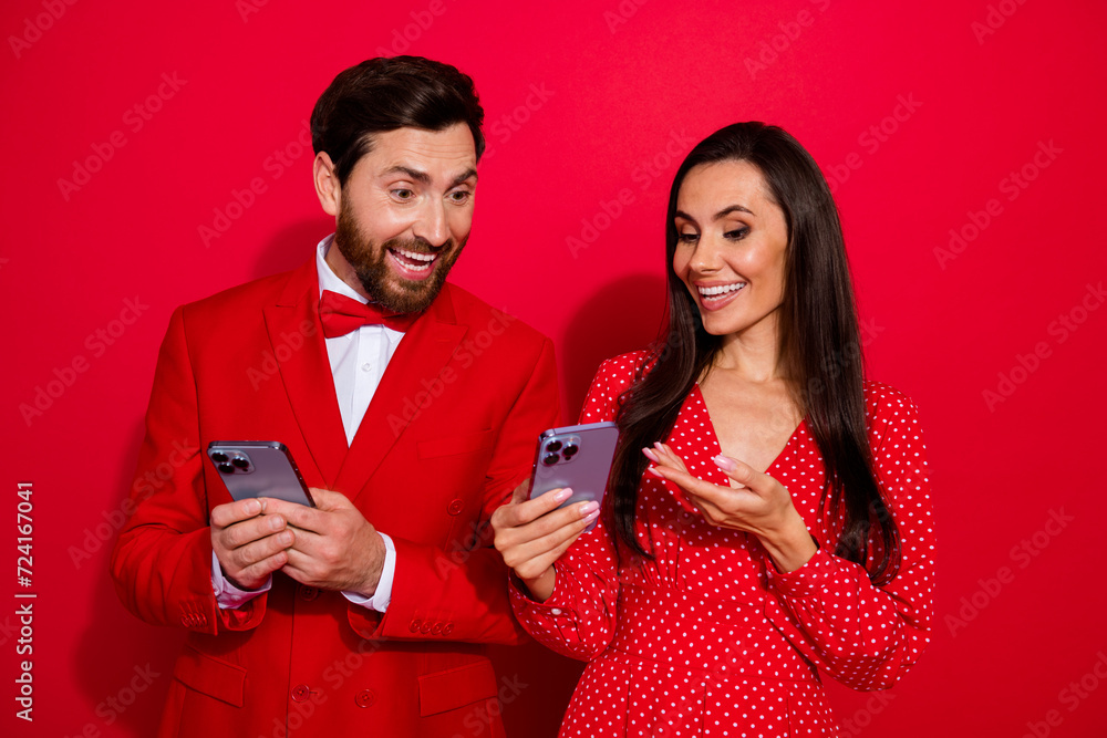 Poster photo of two classy positive people use showing each other smart phone isolated on vibrant red color