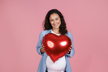 Cheerful pregnant woman holding heart shaped balloon