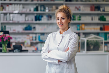 Portrait of a young happy pharmacy shop assistant standing with arms crossed and smiling at the...