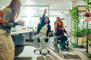 Asian woman racing a woman who uses a wheelchair in an office chair race