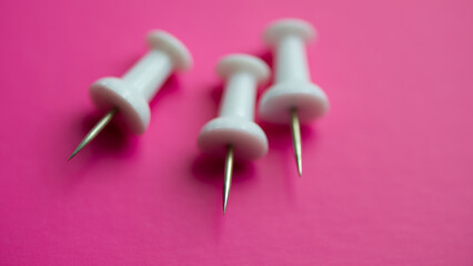 Three white pushpins on pink, close -up.
