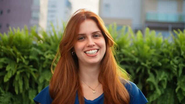 Young woman with sunshine in red hair smiling at the camera. Portrait video of happy lady close up slow motion.