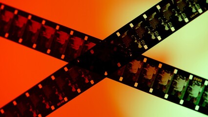 Crossed stripes of photographic film on gradient red orange background close up. Negatives of...