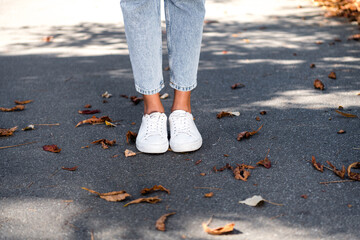 Cropped photo of woman wearing stylish white sneakers standing on asphalt sidewalk walk outside