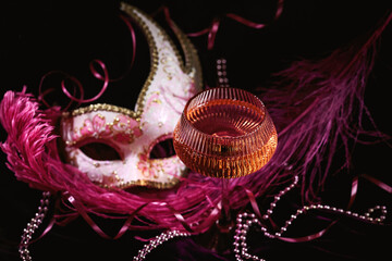 Masquerade ball holiday background. Glass of rose champagne, Venetian carnival mask and feathers on...