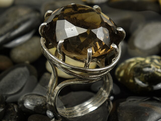Silver ring with smoky topaz on a background of water and black pebbles
