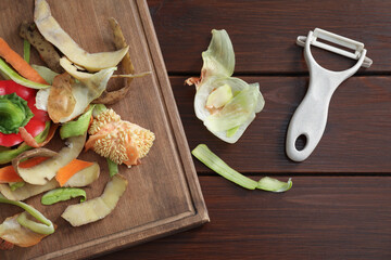 Peels of fresh vegetables and peeler on wooden table, flat lay