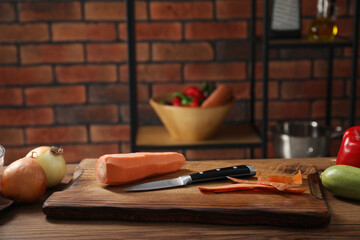Carrot, peels, knife and other vegetables on wooden table in kitchen