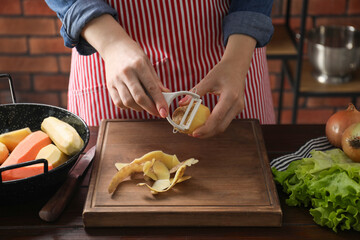 Woman peeling fresh potato at wooden table indoors, closeup