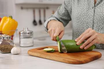 Cooking process. Woman cutting zucchini at white marble countertop in kitchen, closeup