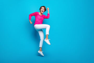 Fototapeta na wymiar Full length photo of positive lucky woman wear knitted neon shirt jumping high rising fists empty space isolated blue color background