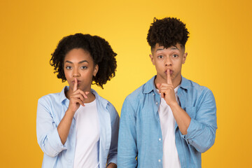 Two young African American individuals signaling silence with a finger over their lips