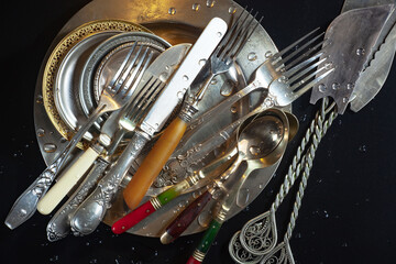 Antique silver cutlery, forks, spoons, knives, in a composition on a black background.