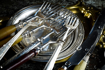 Antique silver cutlery, forks, spoons, knives, in a composition on a black background.