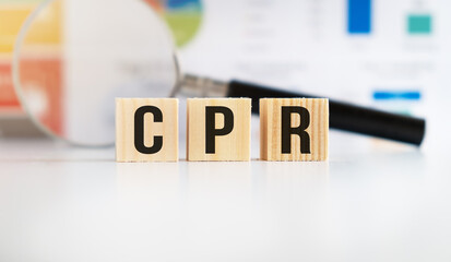 Cubes with letters CPR on white table with magnifier and graphs in background