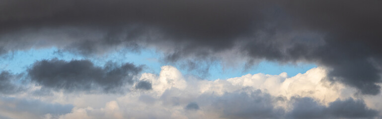 Fototapeta na wymiar A heavy dark cloud hangs over a white cloud in a blue sky
