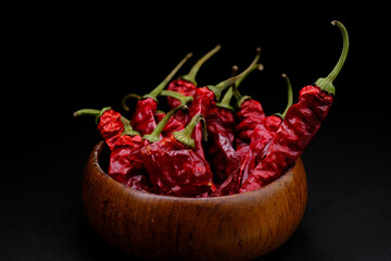 Dry chili peppers in a wooden plate on a black background. Dry vegetables. Dry spices.