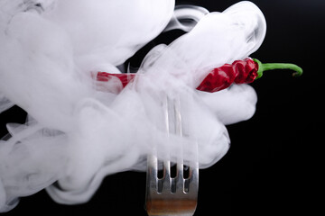 Dry burnt chili pepper on a fork in thick smoke on a black background. Dry vegetables.Close up.