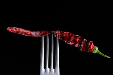 Dried red hot pepper on a fork on a black background close-up
