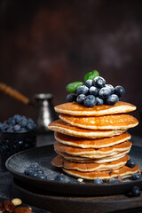 Pile of pancakes with blueberries on a plate on a dark background 