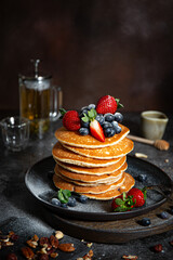 Pile of pancakes with blueberries and strawberries on a plate with dark background  