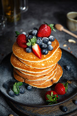 Pile of pancakes with blueberries and strawberries on a plate with dark background  