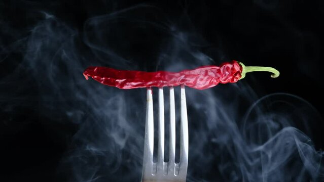 Smoke on a black background with dried red chili peppers on a fork, close-up on a black background in slow motion.