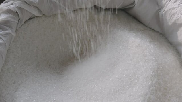 Closeup of a persons hand pouring sugar from a sack showcasing the texture and grains of the sugar
