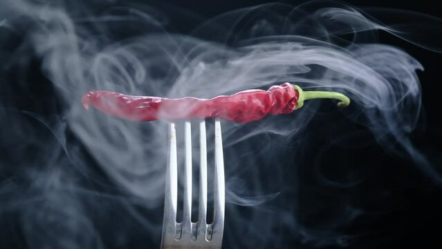 Smoke on a black background with dried red chili peppers on a fork, close-up on a black background in slow motion.