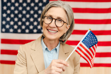 Portrait of smiling confident senior woman, politician holding American flag looking at camera. Vote, United States presidential election concept