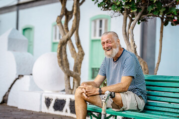 Elderly man with prosthetic leg. left rests sitting on a park bench. Spending a relaxing afternoon. People concept