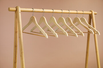 Empty clothes hangers on wooden rack against light brown background