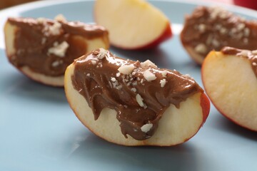 Slices of fresh apple with nut butter and chopped nuts on plate, closeup