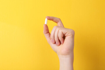 Woman holding vitamin capsule on yellow background, closeup. Space for text