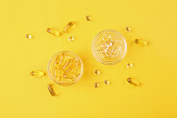 Different vitamin capsules in glass bowls on yellow background, flat lay
